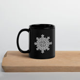 A Xigfireon black glossy 11oz mug featuring the Black & White Solid iteration of the `Morning Star Fire` Celtic knot design sitting on a cutting board. This Celtic knot symbolizes Father Sun.