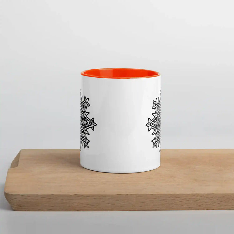 A cutting board displaying a Xigfireon white ceramic 11oz mug featuring the Black & White Solid iteration of the `Morning Star Fire` Celtic knot design, with orange handle and inside. This Celtic knot symbolizes Father Sun.