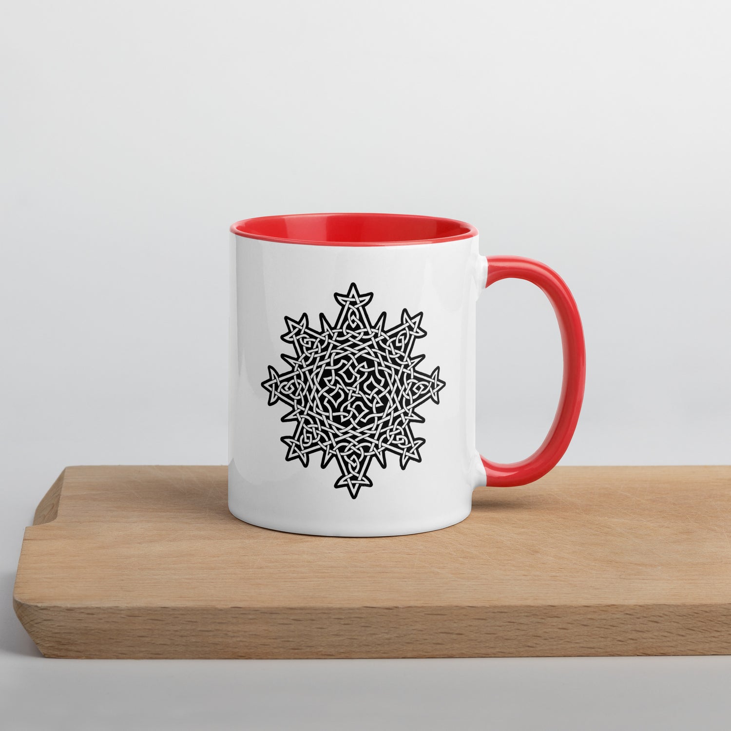 A cutting board displaying a Xigfireon white ceramic 11oz mug featuring the Black & White Solid iteration of the `Morning Star Fire` Celtic knot design, with red handle and inside. This Celtic knot symbolizes Father Sun.