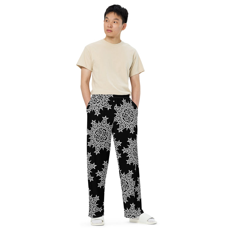 A young man wearing a pair of Xigfireon graphic wide leg pants featuring the Black and White Solid patterned series of the `Morning Star Fire` Celtic knot design.