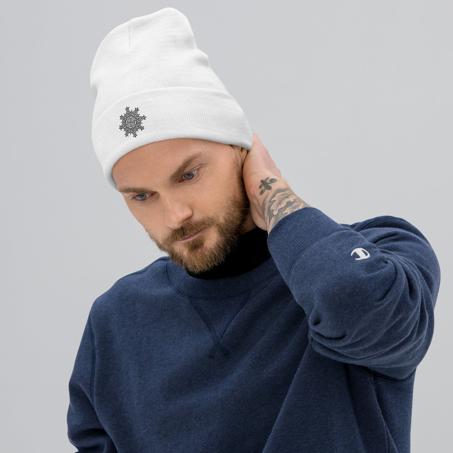 A young man wearing a white Xigfireon knit beanie embroidered with the Black iteration of the `Morning Star Fire` Celtic knot design.