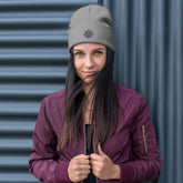 A young woman wearing a grey Xigfireon knit beanie embroidered with the Black iteration of the `Morning Star Fire` Celtic knot design.