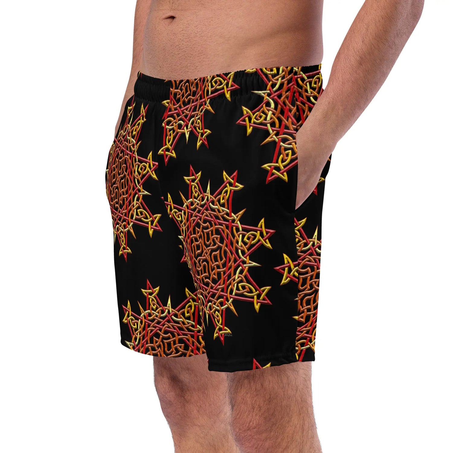 A young man wearing a pair of Xigfireon graphic swim trunks featuring the Fire Colour Black patterned series of the `Morning Star Fire` Celtic knot design.