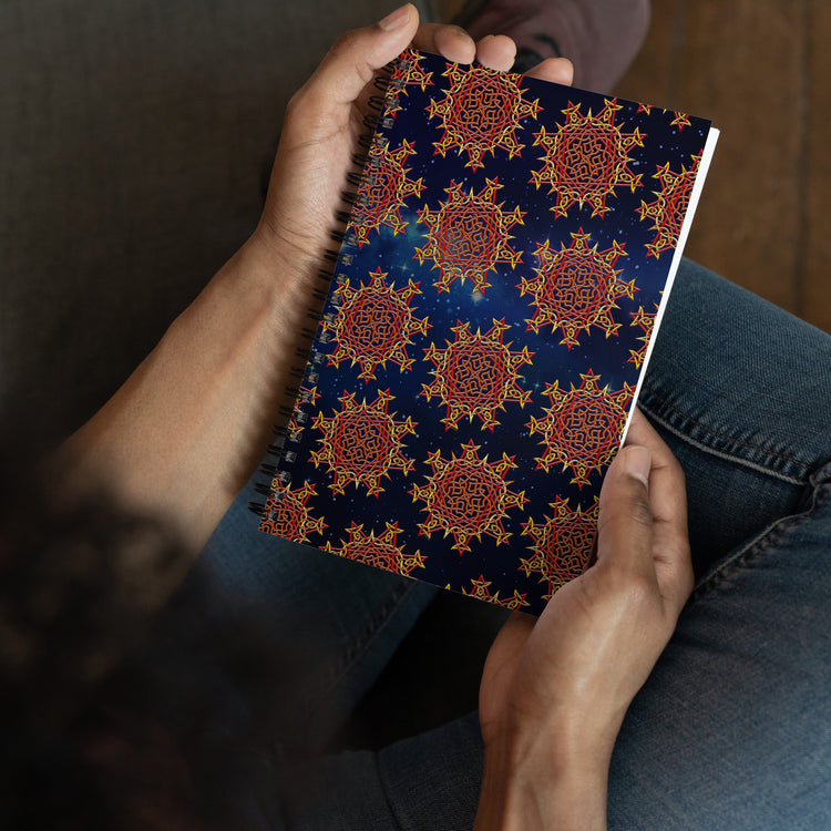 A persons hands shown holding a Xigfireon graphic spiral notebook featuring the Fire Colour Cosmos patterned series of the `Morning Star Fire` Celtic knot design.