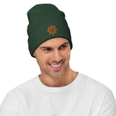 A young man wearing a dark green Xigfireon knit beanie embroidered with the Fire Colour iteration of the `Morning Star Fire` Celtic knot design.