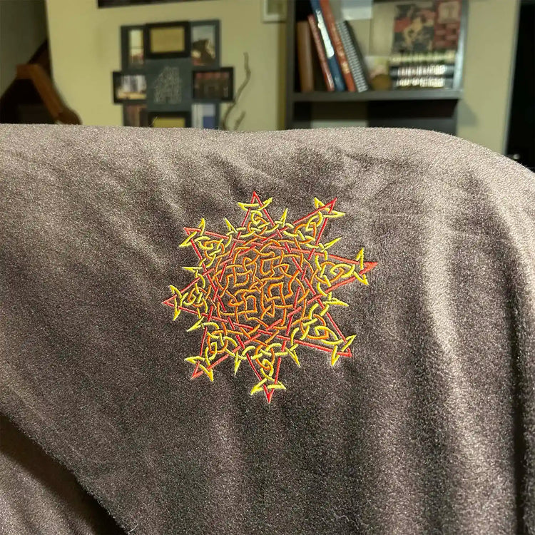 A fireside brown Xigfireon sherpa blanket embroidered with the Fire Colour iteration of the `Morning Star Fire` Celtic knot design. The `Morning Star Fire` Celtic knot represents Father Sun.