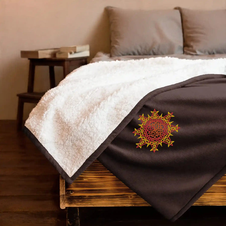 A bed made up with a fireside brown Xigfireon sherpa blanket embroidered with the Fire Colour iteration of the `Morning Star Fire` Celtic knot design.