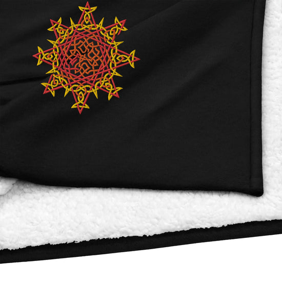 A close-up view of a black Xigfireon sherpa blanket embroidered with the Fire Colour iteration of the `Morning Star Fire` Celtic knot design.