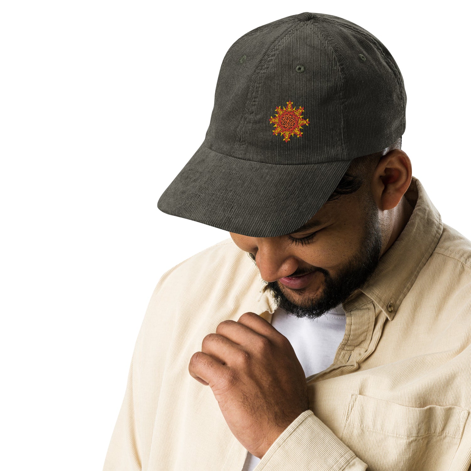 A young man wearing an olive green Xigfireon vintage corduroy cap embroidered with the Fire Colour iteration of the `Morning Star Fire` Celtic knot design offset to the left.