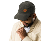 A young man wearing an olive green Xigfireon vintage corduroy cap embroidered with the Fire Colour iteration of the `Morning Star Fire` Celtic knot design offset to the left.