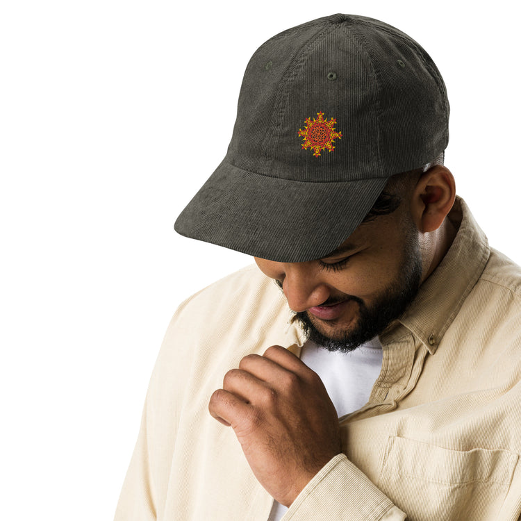 A young man wearing an olive green Xigfireon vintage corduroy cap embroidered with the Fire Colour iteration of the `Morning Star Fire` Celtic knot design offset to the left.