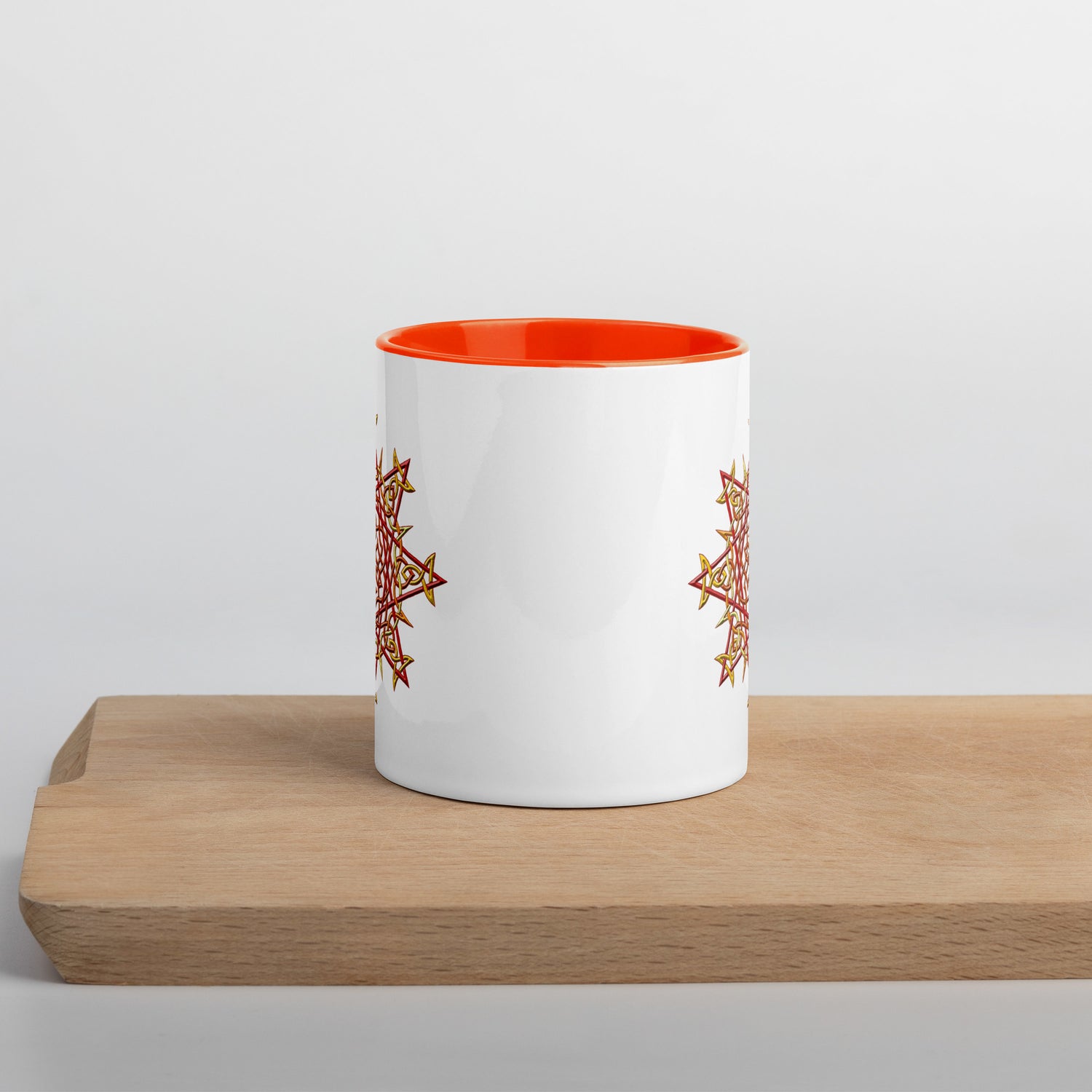 The front side of a Xigfireon white ceramic 11oz mug featuring the Fire Colour iteration of the `Morning Star Fire` Celtic knot design, with orange handle and inside. This Celtic knot symbolizes Father Sun.