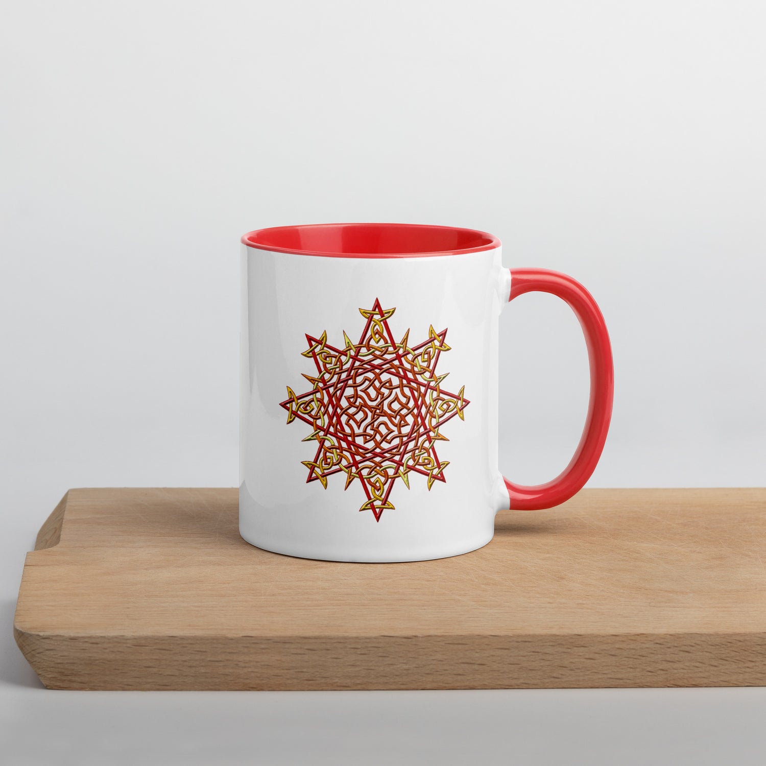 A cutting board displaying a Xigfireon white ceramic 11oz mug featuring the Fire Colour iteration of the `Morning Star Fire` Celtic knot design, with red handle and inside. This Celtic knot symbolizes Father Sun.