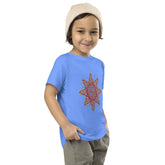 A young boy shown wearing a heather Columbia blue Xigfireon toddler graphic t-shirt featuring the Fire Colour iteration of the `Morning Star Fire` Celtic knot design. The `Morning Star Fire` Celtic knot represents the Sun.