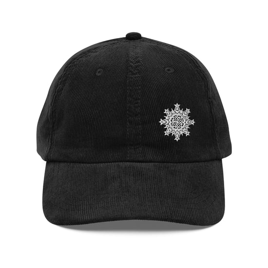 The front side of a black Xigfireon vintage corduroy cap embroidered with the White iteration of the `Morning Star Fire` Celtic knot design offset to the left.