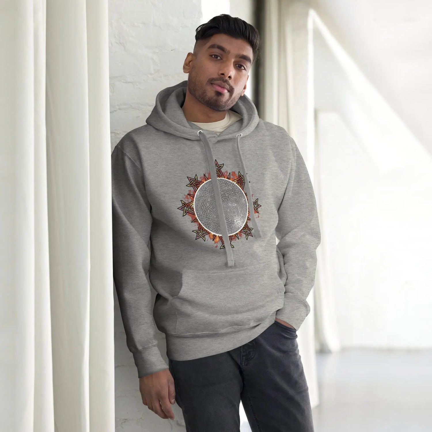 A young man wearing a carbon grey Xigfireon graphic hoodie featuring the Eclipsed iteration of the `Morning Star Fire` Celtic knot design, inspired by the 2023 Annular Solar Eclipse.