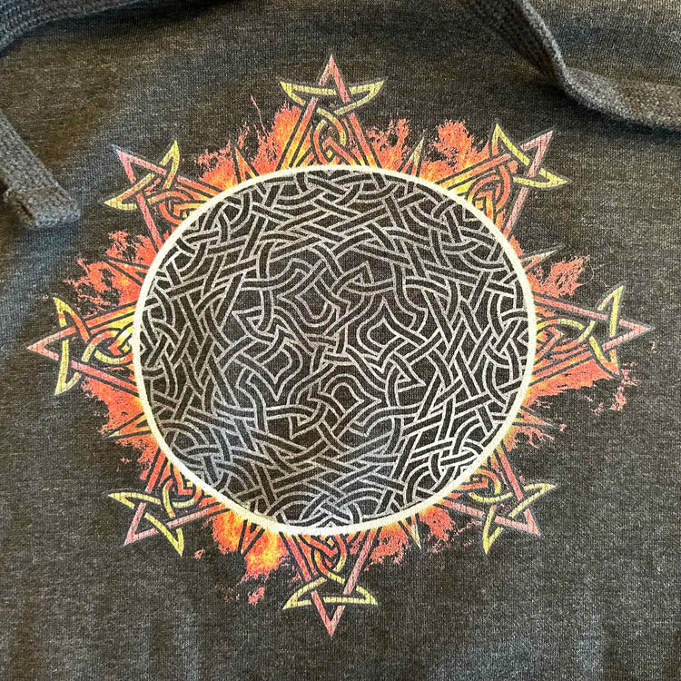 A close-up view of a charcoal heather Xigfireon graphic hoodie featuring the Eclipsed iteration of the `Morning Star Fire` Celtic knot design, inspired by the 2023 Annular Solar Eclipse.