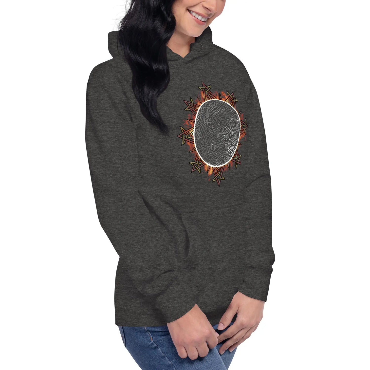 A young woman wearing a charcoal heather Xigfireon graphic hoodie featuring the Eclipsed iteration of the `Morning Star Fire` Celtic knot design, inspired by the 2023 Annular Solar Eclipse.