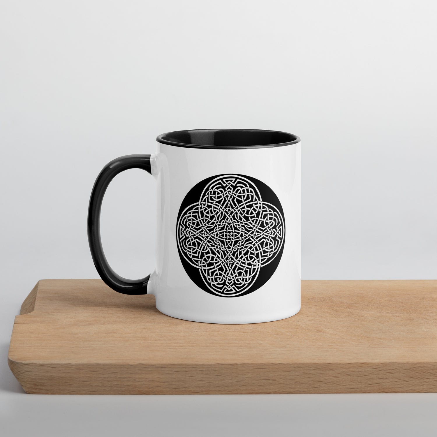 A Xigfireon white ceramic 11oz mug featuring the Black & White Circle iteration of the `Reach Of The Spirit` Celtic knot design, with black handle and inside. This Celtic knot symbolizes Mother Earth.