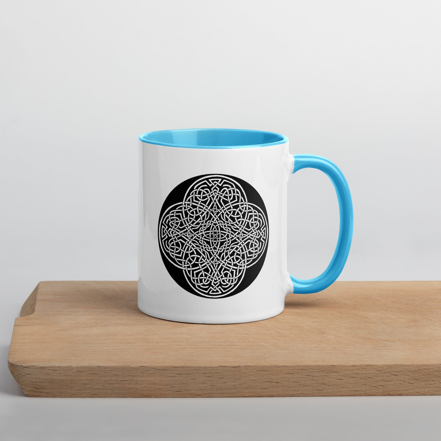 A Xigfireon white ceramic 11oz mug featuring the Black & White Circle iteration of the `Reach Of The Spirit` Celtic knot design, with blue handle and inside. This Celtic knot symbolizes Mother Earth.