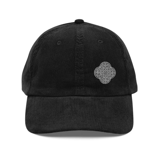 A young woman wearing a black Xigfireon vintage corduroy cap embroidered with the Black & White Solid iteration of the `Reach Of The Spirit` Celtic knot design offset to the left.