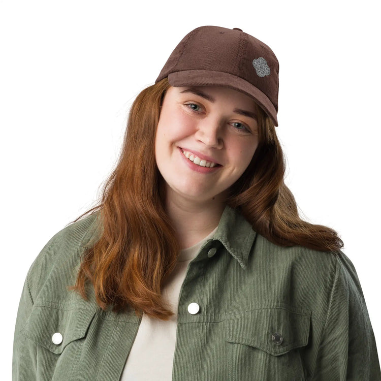 A young woman wearing a brown Xigfireon vintage corduroy cap embroidered with the Black & White Solid iteration of the `Reach Of The Spirit` Celtic knot design offset to the left.