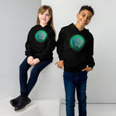 A young girl and a young boy, each wearing a black graphic hoodie featuring the Deep Forest iteration of the `Reach Of The Spirit` Celtic knot design.