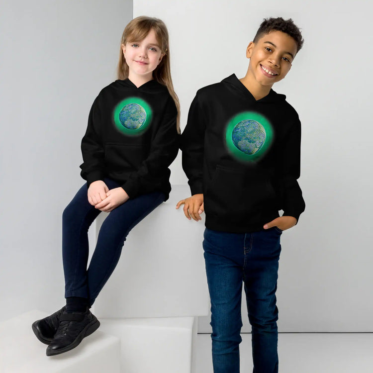 A young girl and a young boy, each wearing a black graphic hoodie featuring the Deep Forest iteration of the `Reach Of The Spirit` Celtic knot design.