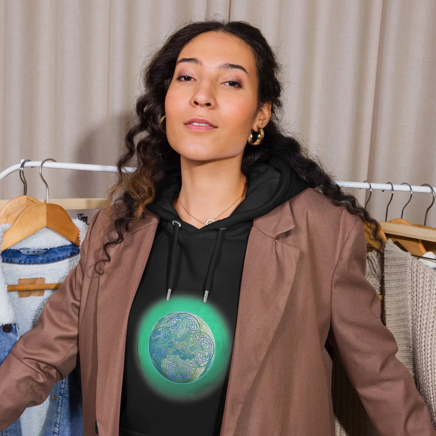 A young woman wearing a black Xigfireon graphic eco-friendly hoodie featuring the Deep Forest iteration of the `Reach Of The Spirit` Celtic knot design. The `Reach Of The Spirit` Celtic knot symbolizes our beautiful Mother Earth.