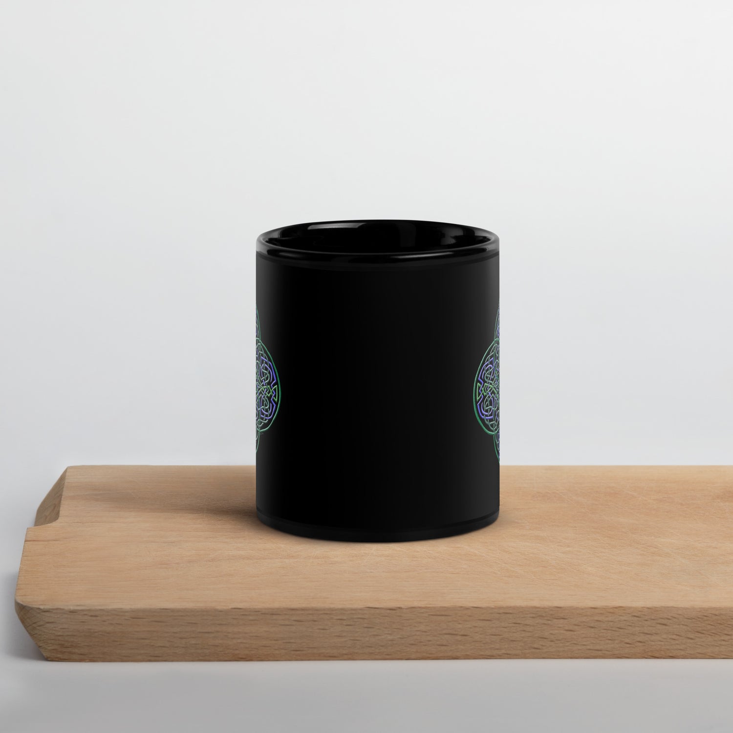 A cutting board displaying a Xigfireon black ceramic 11oz mug featuring the Living Colour iteration of the `Reach Of The Spirit` Celtic knot design. This Celtic knot symbolizes Mother Earth.