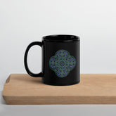 A cutting board displaying a Xigfireon black ceramic 11oz mug featuring the Living Colour iteration of the `Reach Of The Spirit` Celtic knot design. This Celtic knot symbolizes Mother Earth.