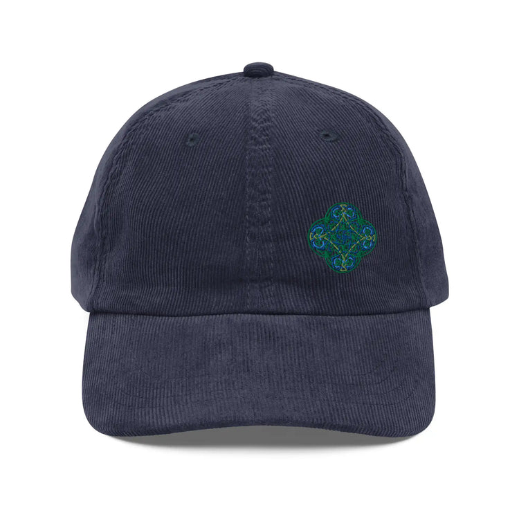 The front side of a navy blue Xigfireon vintage corduroy cap embroidered with the Living Colour iteration of the `Reach Of The Spirit` Celtic knot design offset to the left.