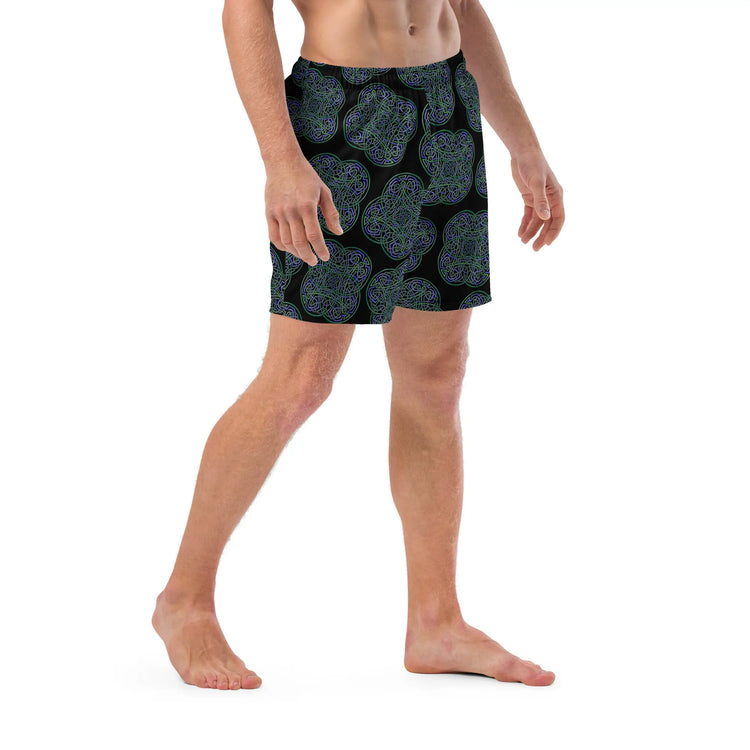 A young man wearing a pair of Xigfireon graphic swim trunks featuring the Living Colour Black (small) patterned series of the `Reach Of The Spirit` Celtic knot design.