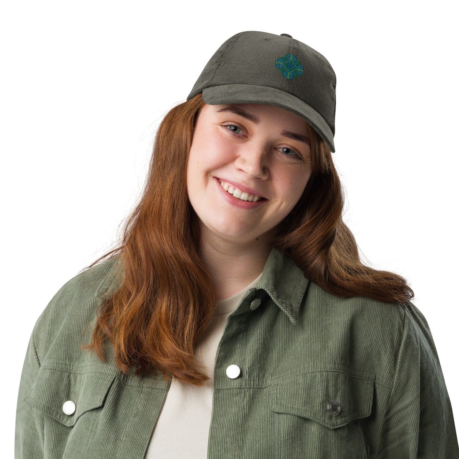 A young woman wearing an olive green Xigfireon vintage corduroy cap embroidered with the Living Colour iteration of the `Reach Of The Spirit` Celtic knot design.