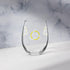 The front side of a stemless wine glass featuring the White & Gold iteration of the Trinity Knot design shown on a counter in front of a textured wall. Also referred to as the triquetra, the Trinity Knot has long symbolized unity and balance.