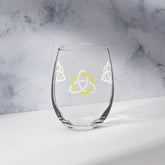 The front side of a stemless wine glass featuring the White & Yellow iteration of the Trinity Knot design shown on a counter in front of a textured wall. Also referred to as the triquetra, the Trinity Knot has long symbolized unity and balance.