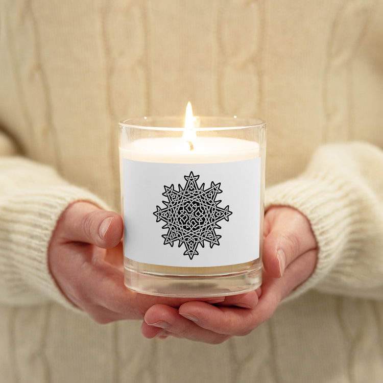 A person holding a Xigfireon glass jar soy wax candle featuring the Black & White Solid iteration of the `Morning Star Fire` Celtic knot design. The `Morning Star Fire` Celtic knot symbolizes Father Sun.