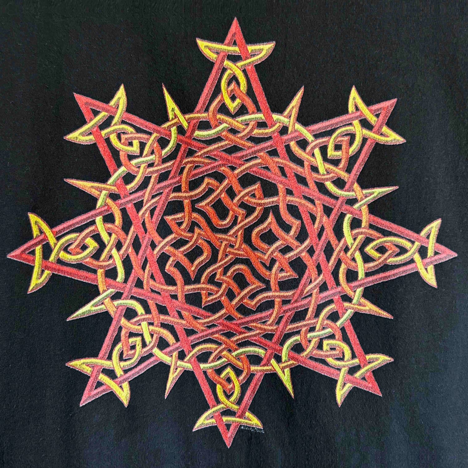 A close-up view of a black Xigfireon graphic t-shirt featuring the Fire Colour iteration of the `Morning Star Fire` Celtic knot design. The `Morning Star Fire` Celtic knot represents Father Sun and the eternal Cosmic Light.