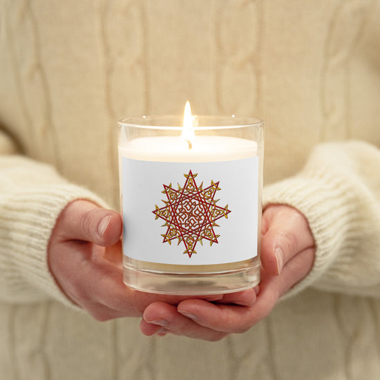 A persons hands holding a Xigfireon glass jar soy wax candle featuring the Fire Colour iteration of the `Morning Star Fire` Celtic knot design. The `Morning Star Fire` Celtic knot symbolizes Father Sun.