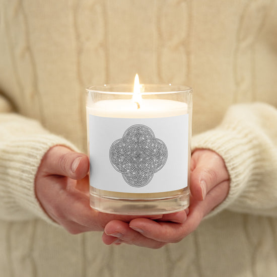 A person holding a Xigfireon glass jar soy wax candle featuring the Black & White Hollow iteration of the `Reach Of The Spirit` Celtic knot design. The `Reach Of The Spirit` Celtic knot symbolizes Mother Earth.