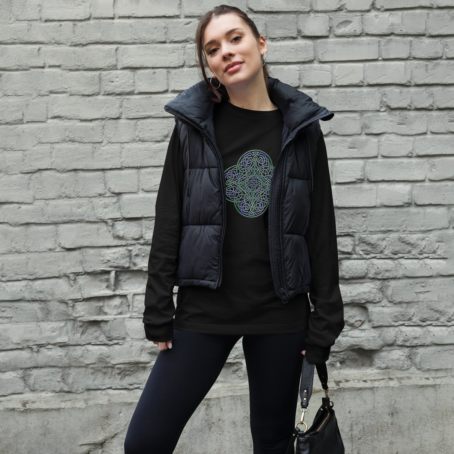 A young woman wearing a black Xigfireon long sleeve graphic t-shirt featuring the Living Colour iteration of the `Reach Of The Spirit` Celtic knot design. The `Reach Of The Spirit` Celtic knot symbolizes Mother Earth.